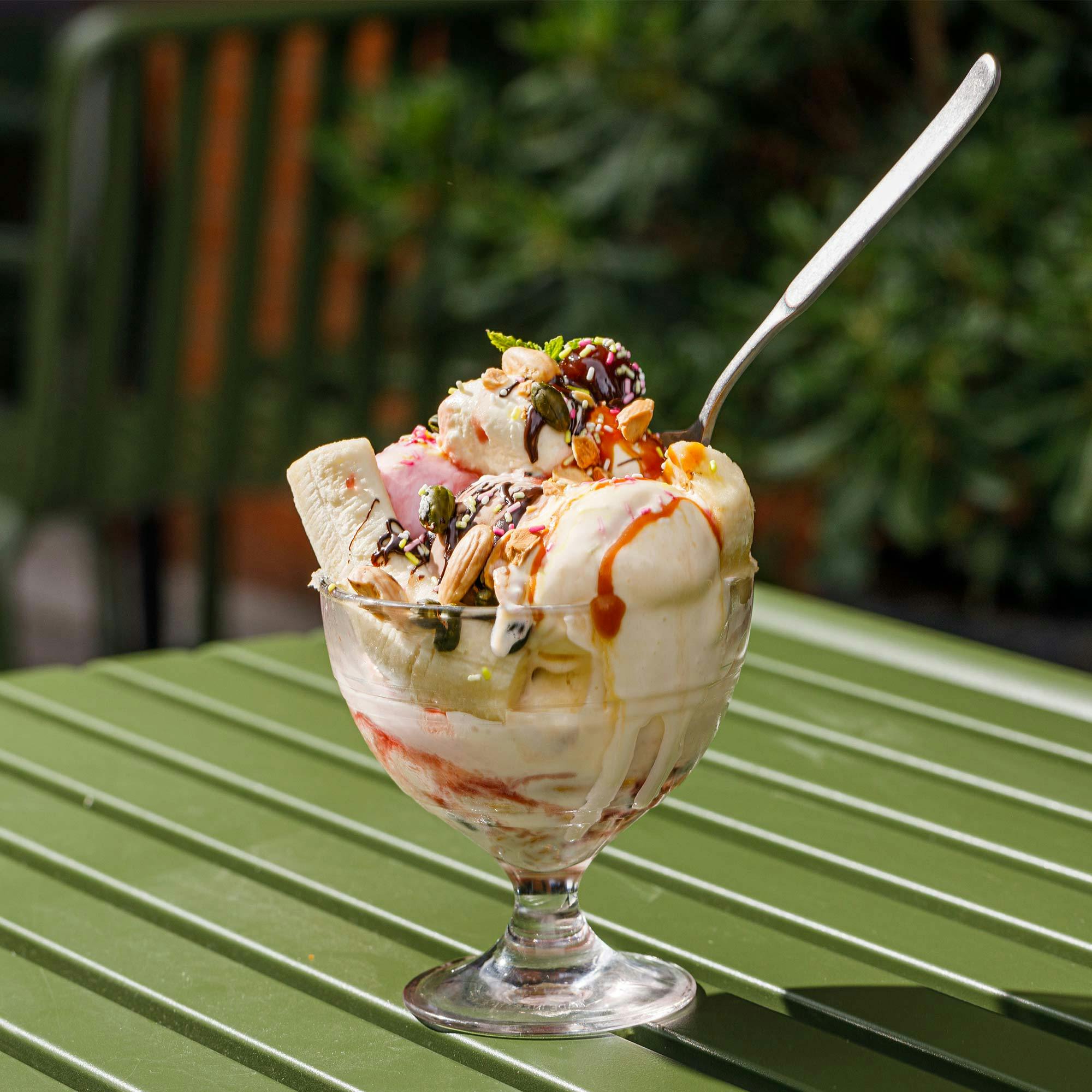 Scrumptious ice cream sundae with bananas, nuts and syrup served outdoors on a sunny day.